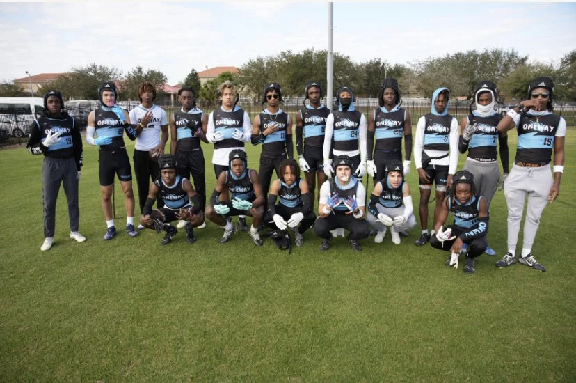 Group of young football players standing and kneeling on a grassy field, wearing matching uniforms and posing for a team photo.