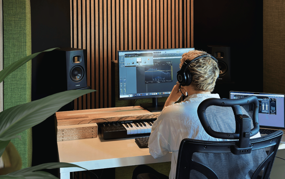 Person i en ljudstudio med datorer och högtalare, arbetar med musikproduktion.
