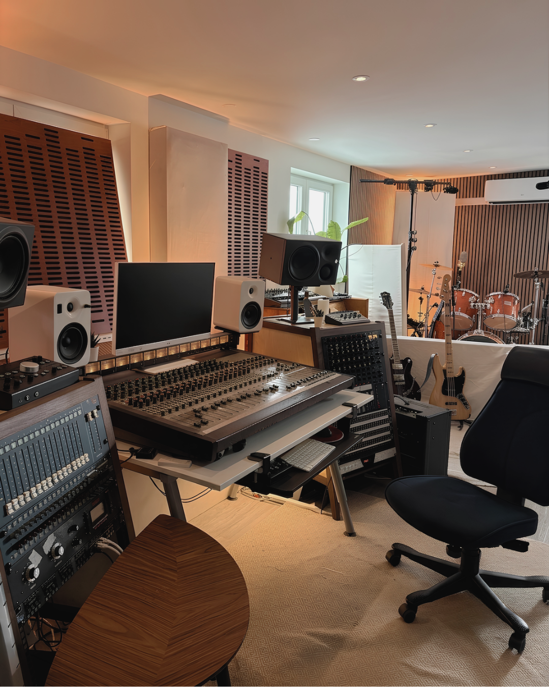 Inuti ett musikstudio med ljudutrustning, gitarrer och ett trumset i bakgrunden.
