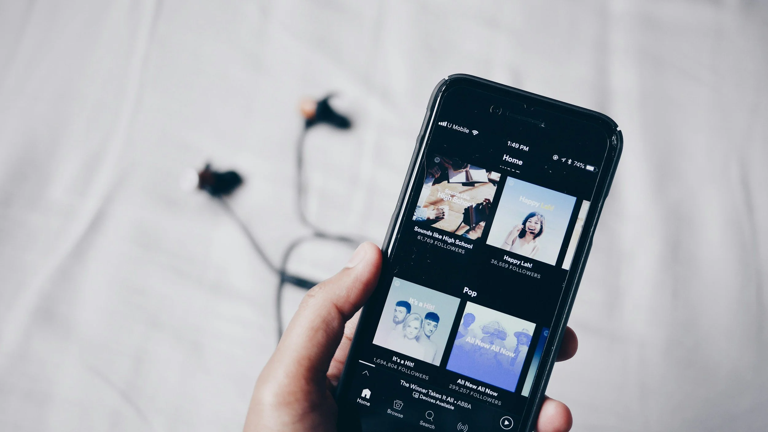 En person håller i en smartphone som visar en app för musik, med spellistor och följare. I bakgrunden syns ett vitt golv.