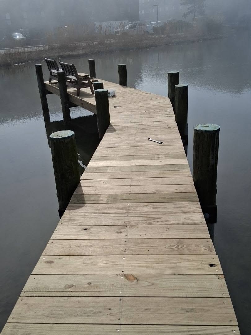Wooden dock with two benches extending over a calm body of water on a foggy day.