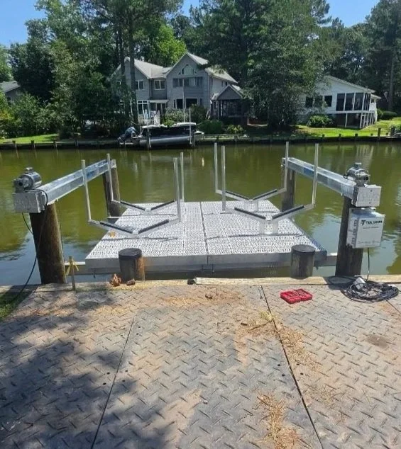 Empty boat dock with metal floating platform on a river, with houses and trees in the background.