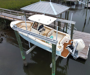 A boat docked at a marina under a covered pavilion, with a white and beige boat featuring a T-top and an outboard motor.