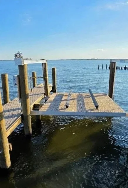 A wooden dock extending into a body of water with a partially damaged section, under a blue sky with some clouds.