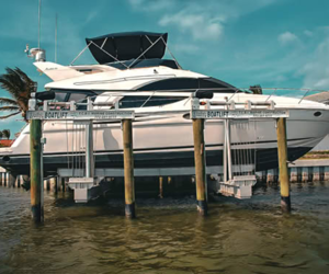 A large white luxury yacht docked at a marina with wooden pilings and a clear blue sky.