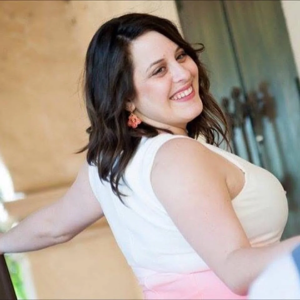 Author Donna Bollen headshot. A dark-haired, smiling woman wearing a white dress against a stone backdrop.