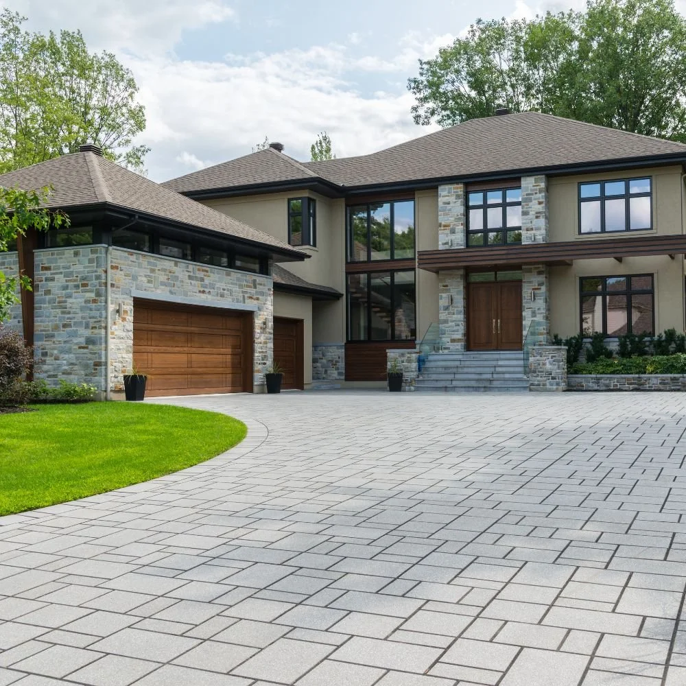 Modern house with stone and stucco exterior, large windows, and wooden accents, surrounded by a well-maintained lawn and a paved driveway.
