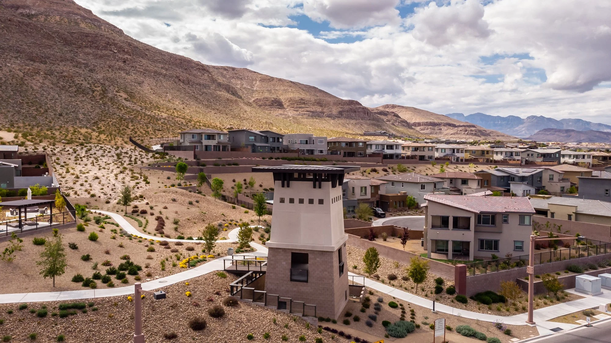 Suburban neighborhood with modern houses, landscaped yards, and a mountain backdrop under cloudy skies.