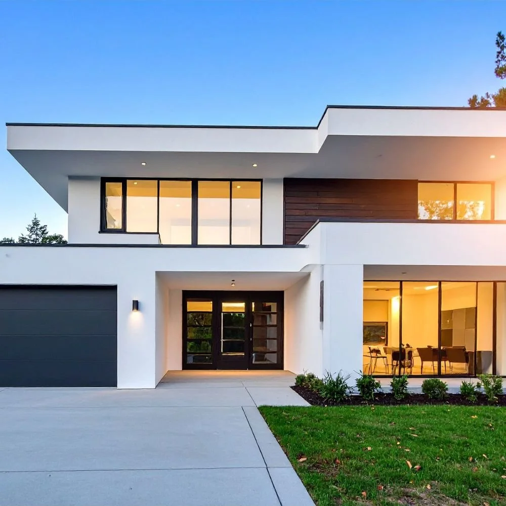 Modern two-story house with large windows, a black garage door, and a small front lawn during sunset.