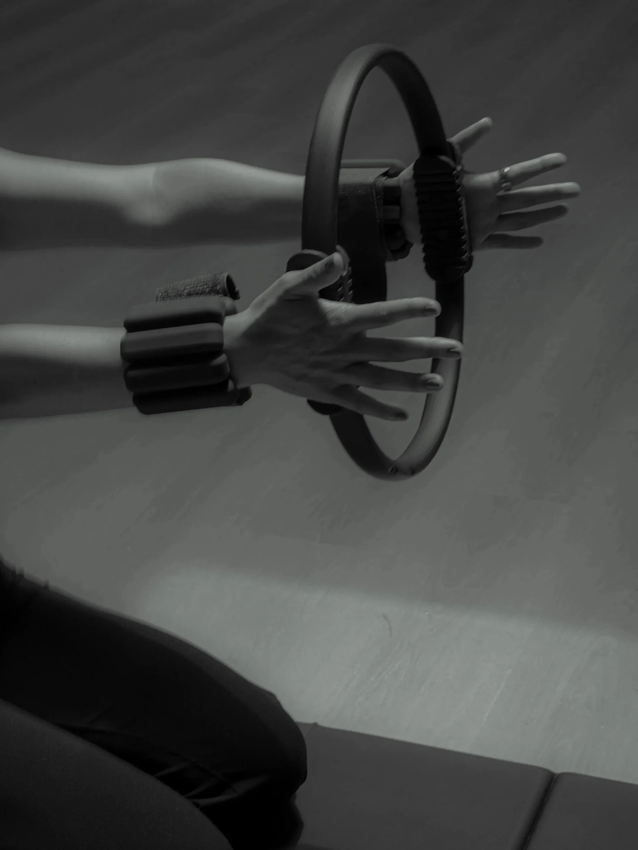 Black-and-white image of a woman toning her arms by pulsing on a Pilates ring.