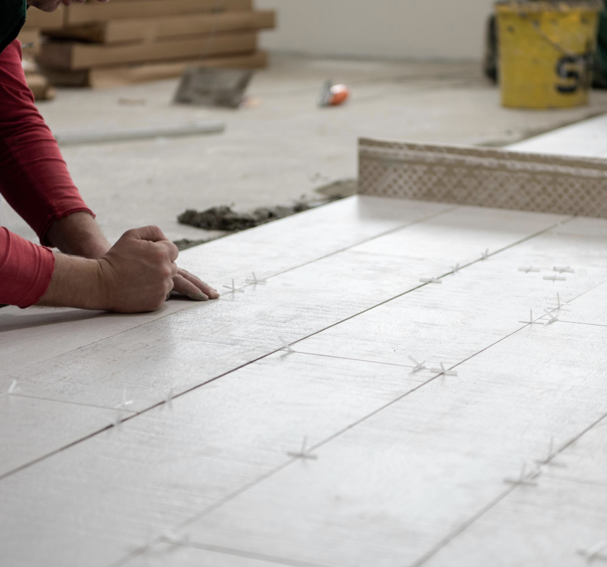 A person installing large tiles on a floor using spacers to ensure even placement in a construction site.