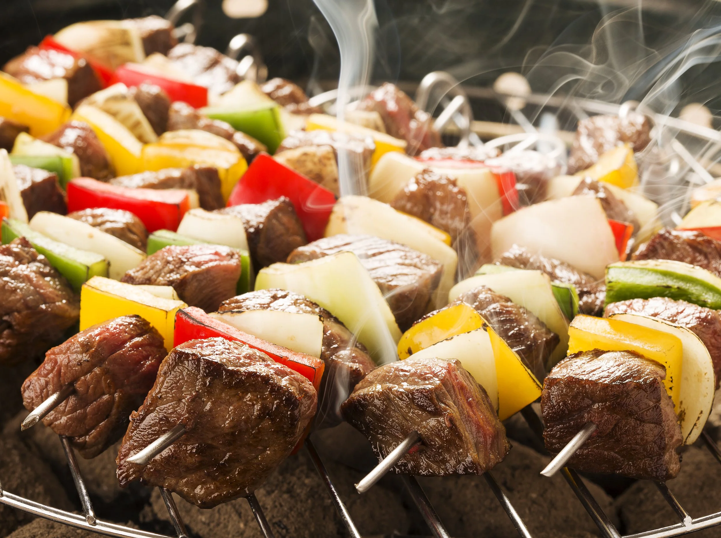 Barbecue skewers with chunks of beef, bell peppers, and onions grilling over a barbecue