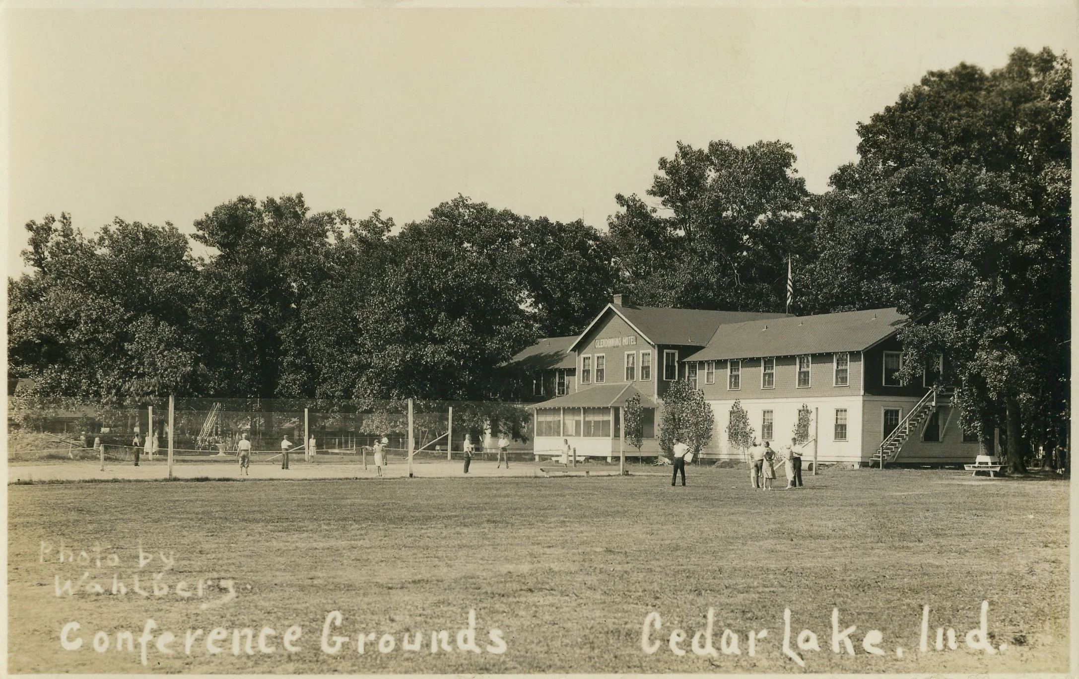 Historic black-and-white photograph of the Clementine Hotel at Cedar Lake, Indiana, with people playing volleyball outside and tall trees behind the building.
