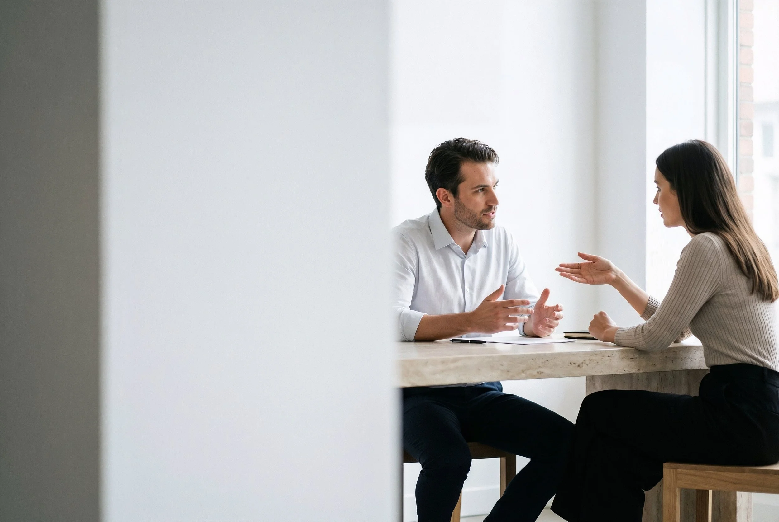 A man and a woman seated at a table, engaged in a coaching conversation, with the woman gesturing with her hand. Representing a personal, yet effective engagement.