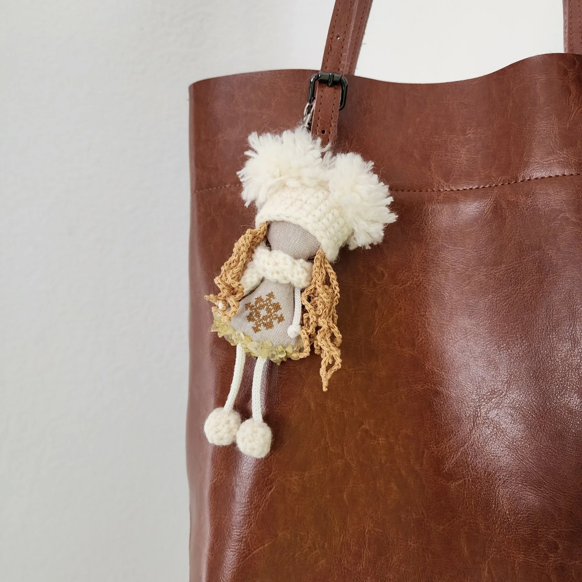 Cream and gold OMmi hanging from a brown leather tote bag, showing its size and use as a personal bag companion.