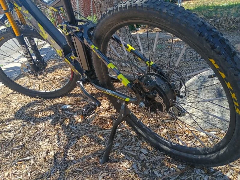 Mountain bike lying on the ground with front wheel partially visible, on a dirt and leaf-covered outdoor ground.