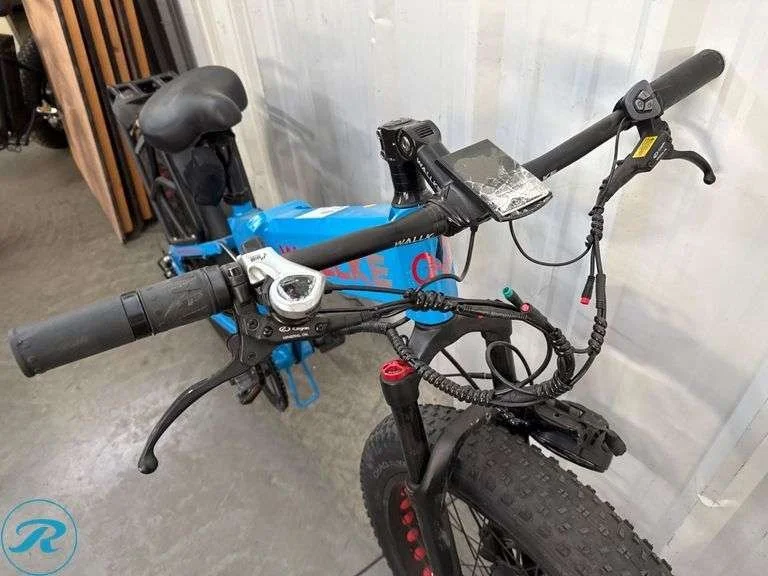 Electric mountain bike with black frame, flat handlebars, and fat tires, parked indoors against a white wall.