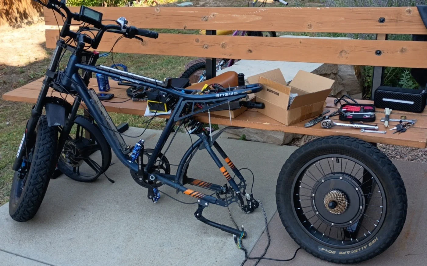 Disassembled electric bicycle on a concrete surface with tools and parts on a wooden bench.