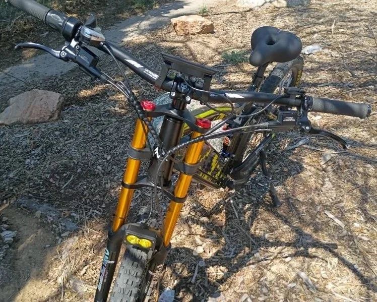 A mountain bike with a black frame and yellow suspension forks on a dirt trail with rocks and trees.