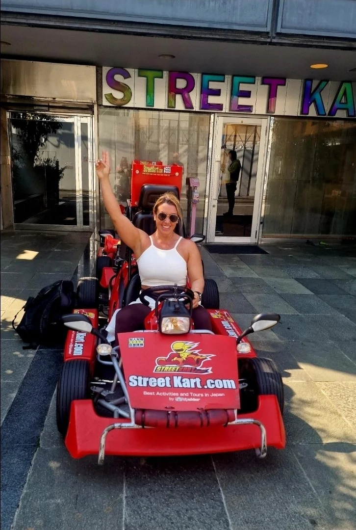 Woman sitting in a red go-kart with a sticker that reads 'Street Kart.com' in front of a store with colorful letters spelling 'Street Kart'.