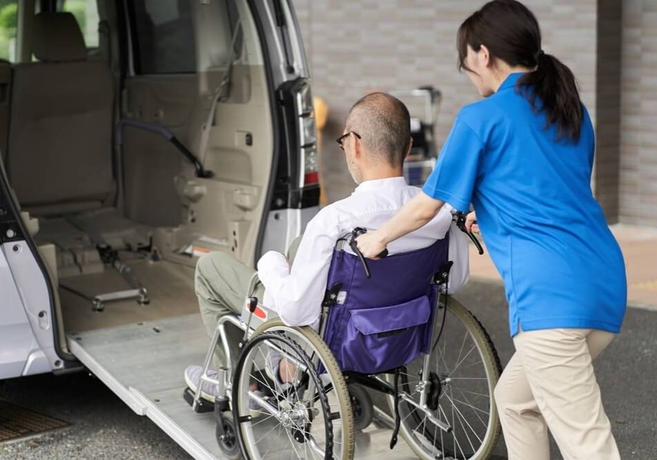A caregiver assisting a man in a wheelchair into a vehicle with a lowered ramp.