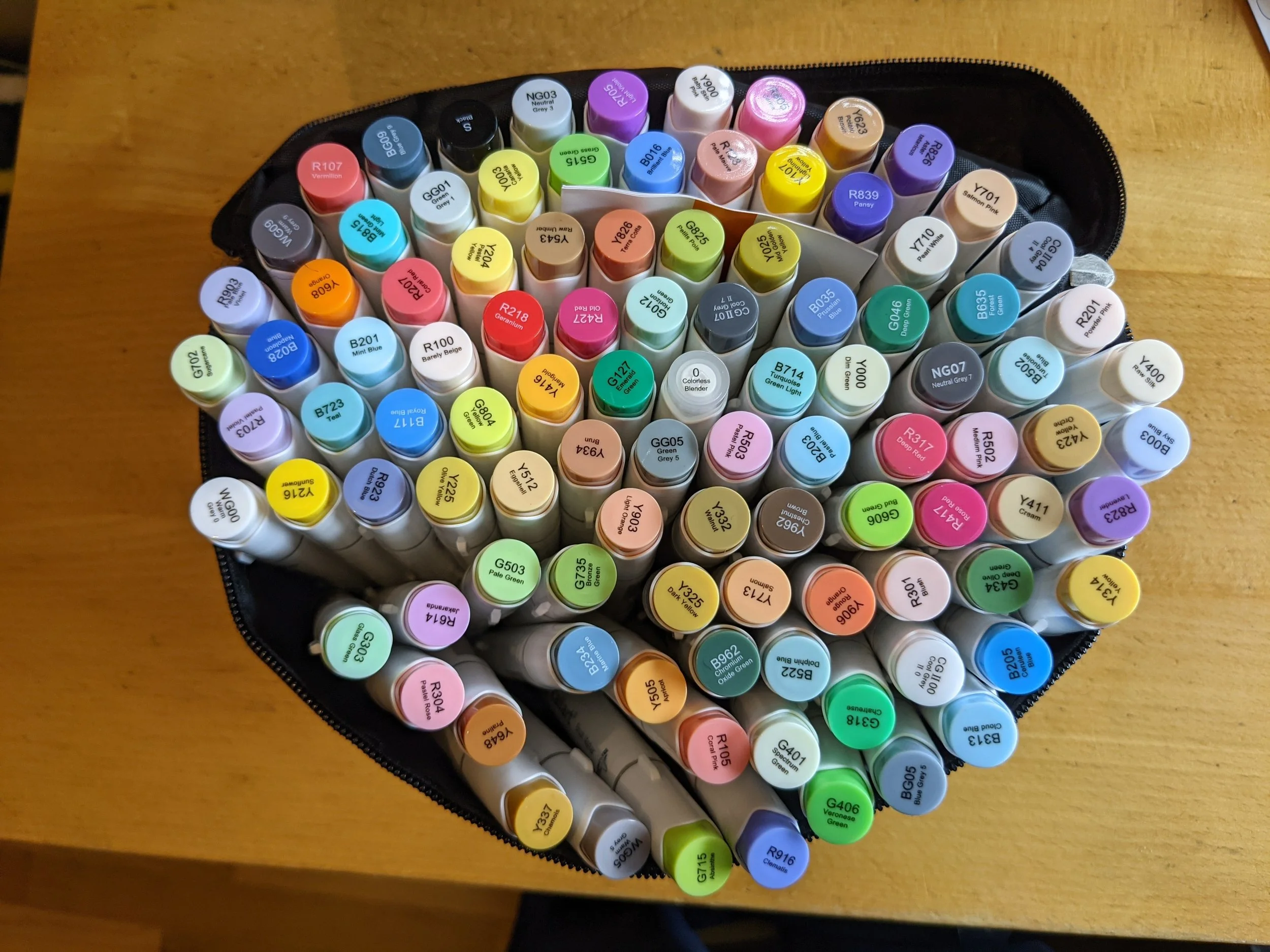 A top view of a pencil case filled with colorful markers arranged in rows on a wooden surface.