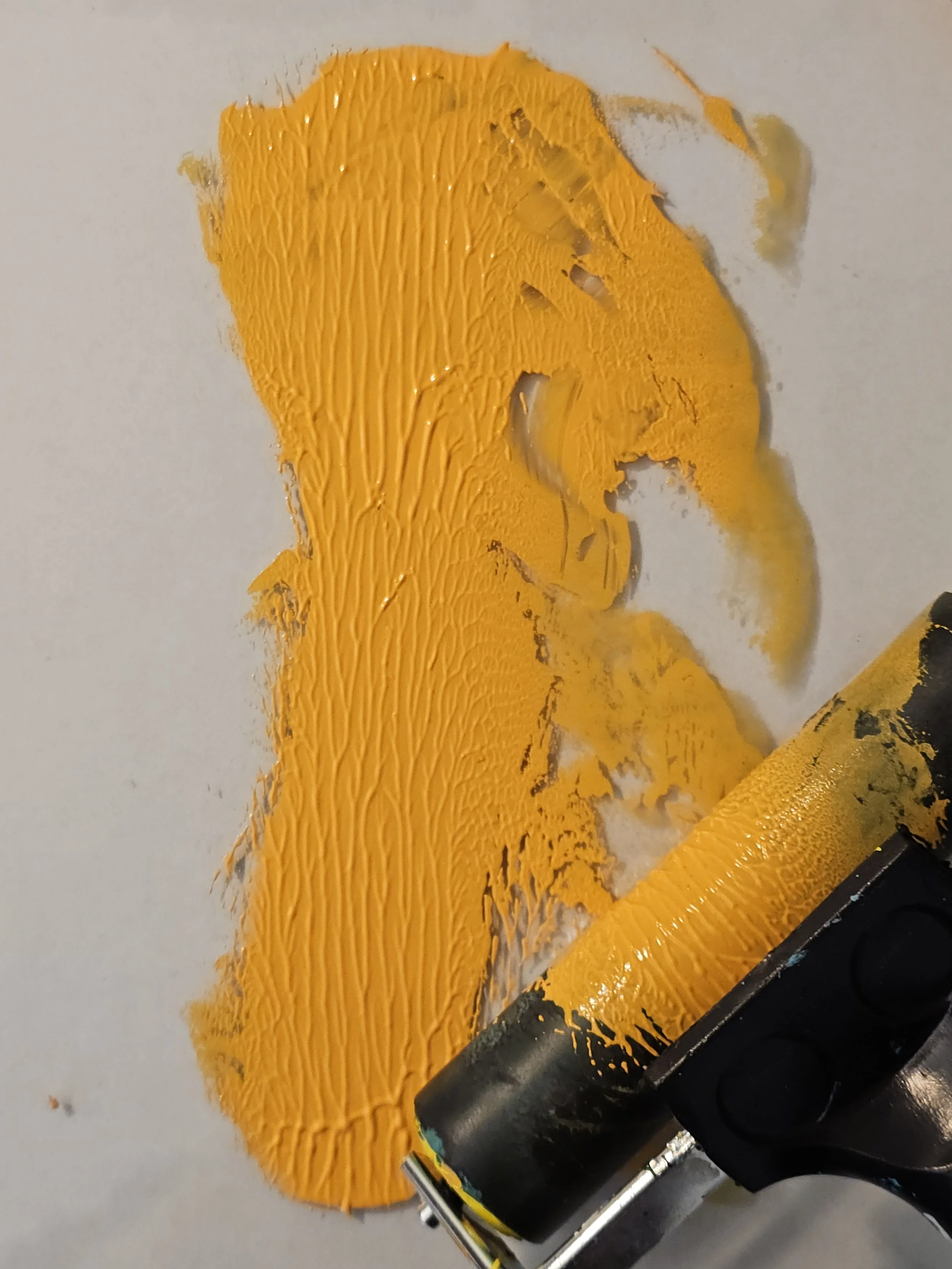 Close-up of yellow and black paint being applied with a roller brush on a smooth surface.
