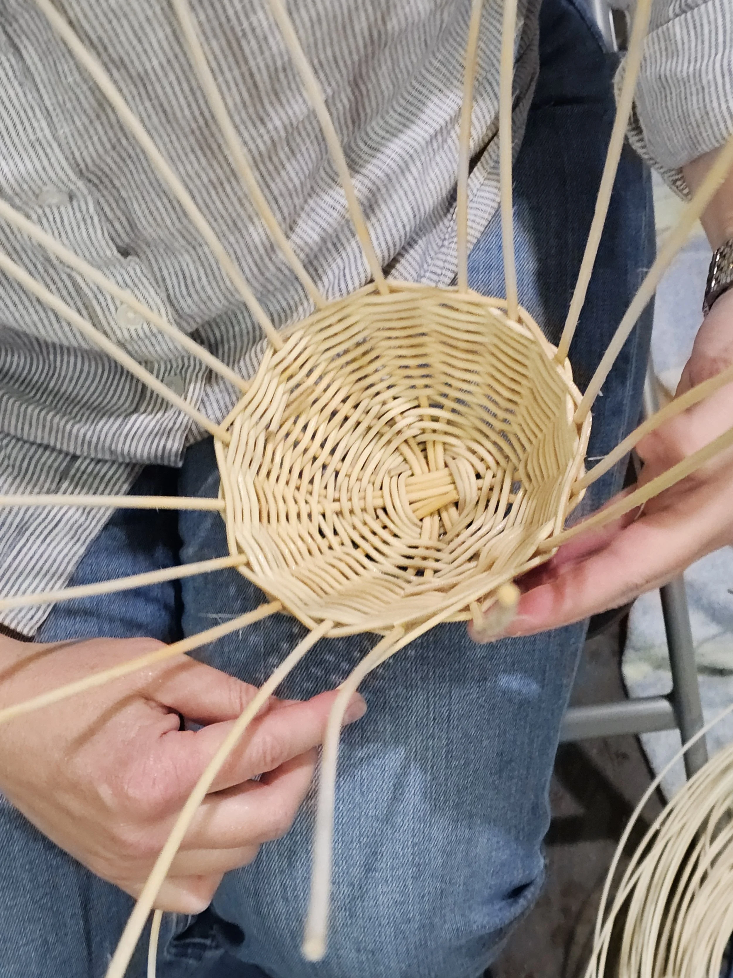 Close-up of hands weaving a light-colored wicker basket with thin wooden strips.