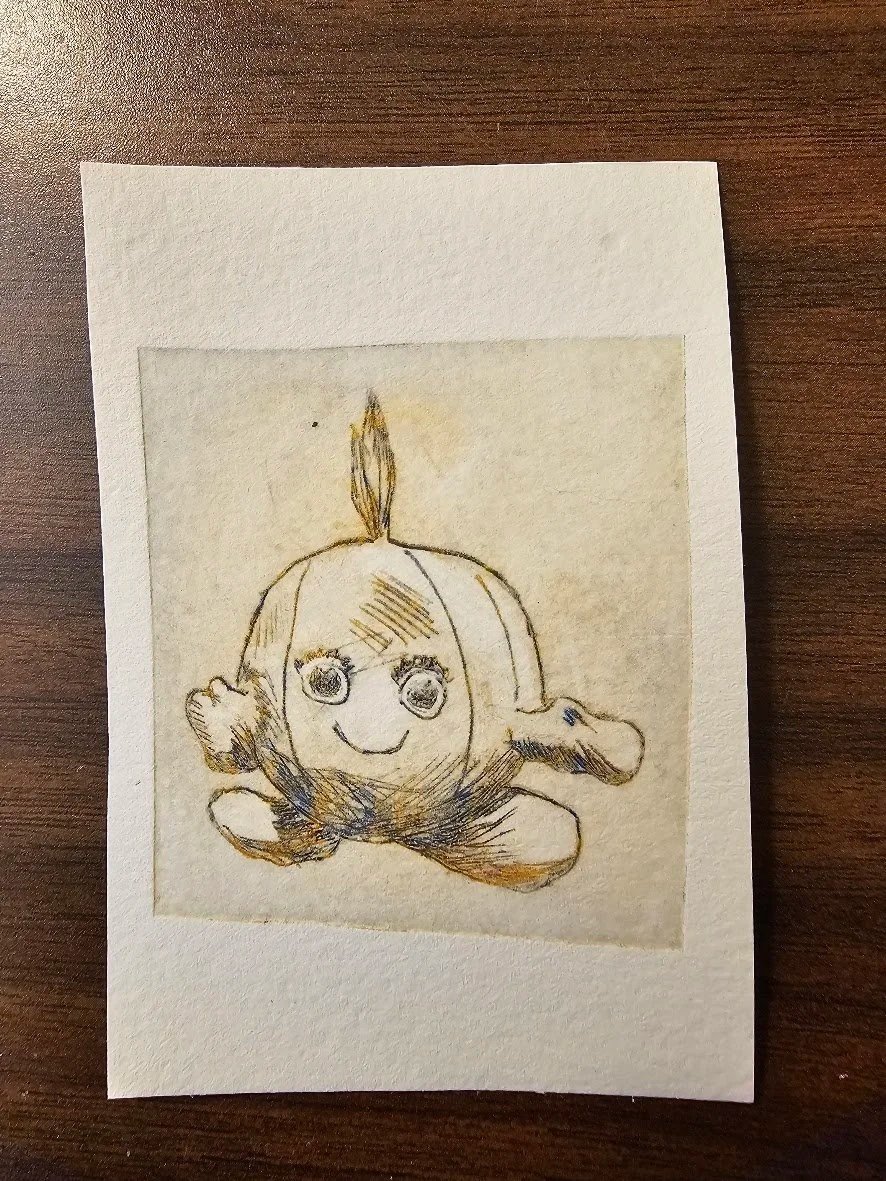 Hand-drawn sketch of a smiling onion with big eyes, arms, and legs, on a piece of paper with a white border, placed on a wooden surface.