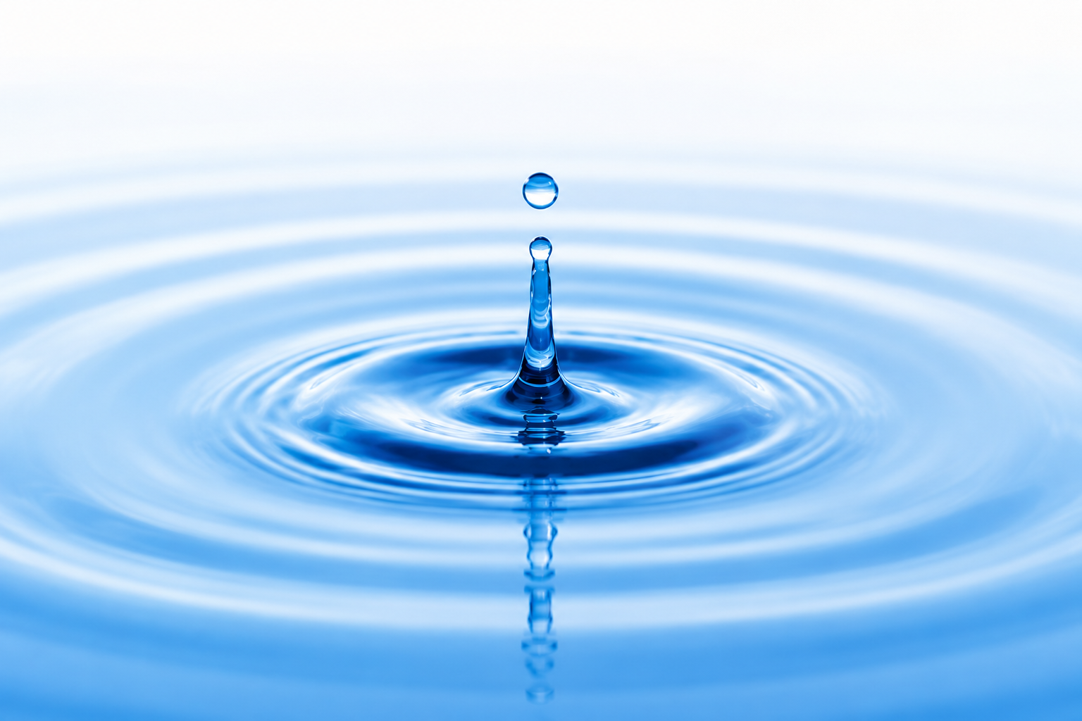 Close-up of a water droplet creating a splash and ripples on a blue water surface.