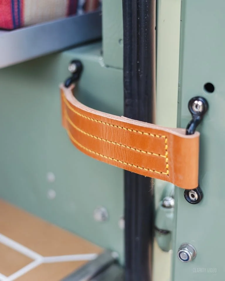 Close-up of a leather strap handle attached to a green metal machine with screws, part of a bookshelf or storage unit.