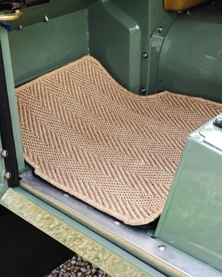 Close-up of a textured beige woven mat on the footwell of a vintage green vehicle.