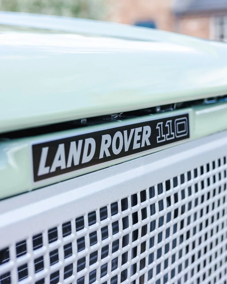 Close-up of a Land Rover 110 badge on the front grille of a white vehicle.