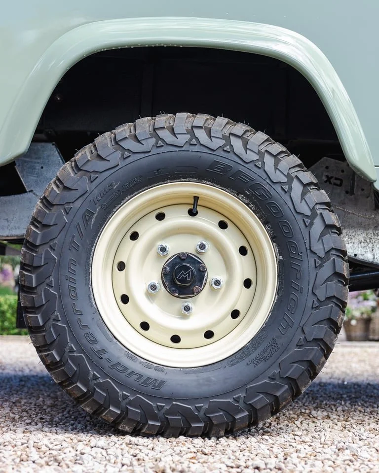 Close-up of a large off-road tire mounted on a cream-colored rim on a vehicle, with part of the green fender visible above.