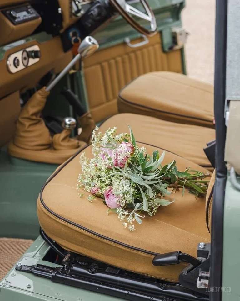 A bouquet of pink peonies, white baby's breath, and greenery resting on the tan seat of a vintage green car interior.