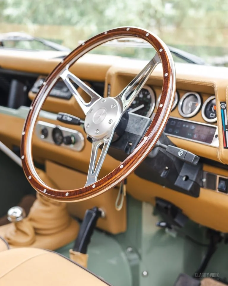 Interior of a vintage vehicle with a wooden steering wheel, tan dashboard, and multiple gauges.