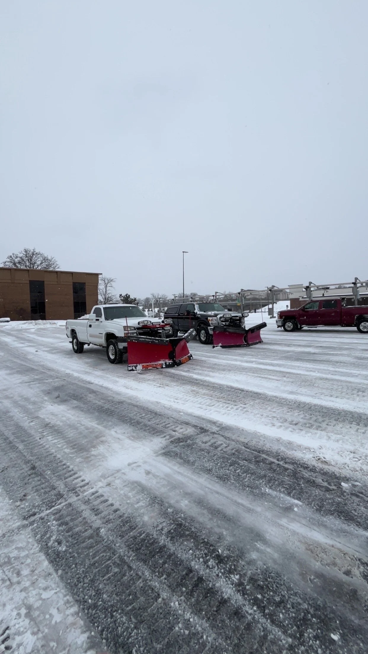 Vehicles with snow plows attached parked on a snow-covered parking lot during winter.