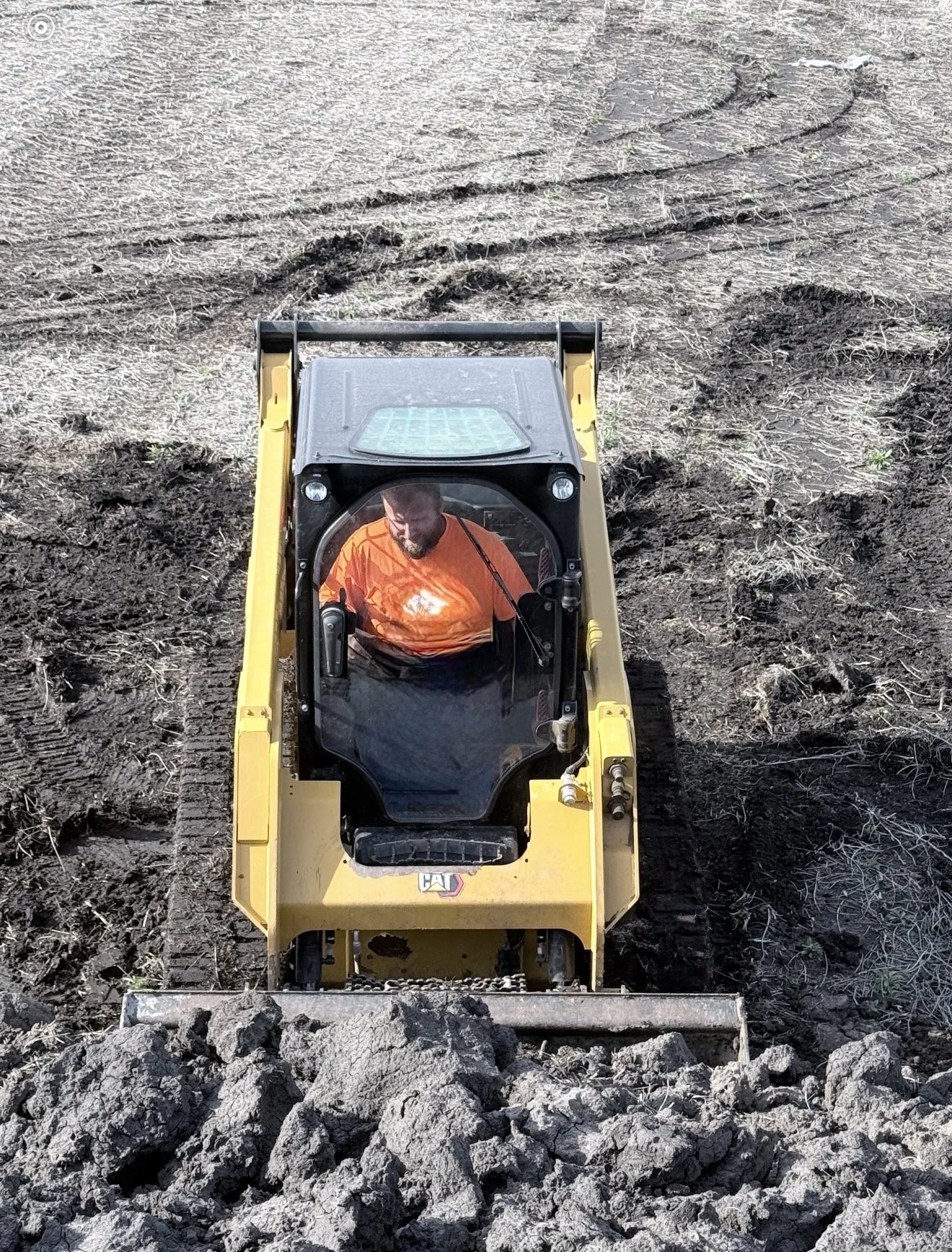 A man driving a small yellow bulldozer, moving large rocks in a dirt field.