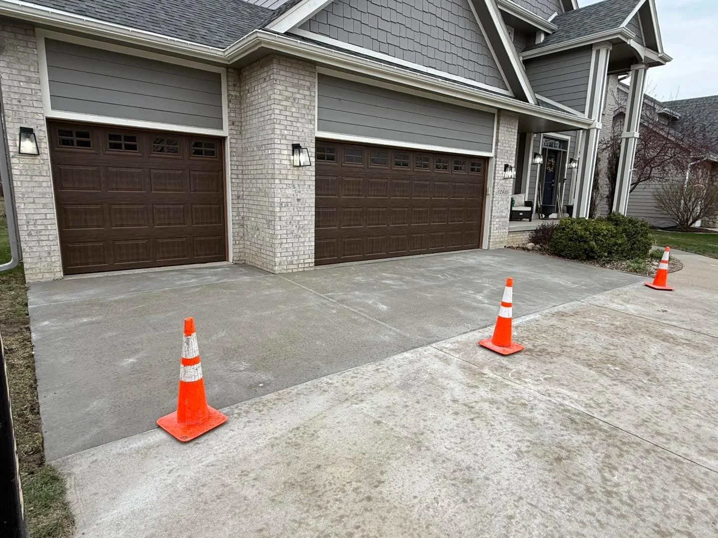 A house with a concrete driveway, three closed garage doors, and orange traffic cones indicating ongoing work.