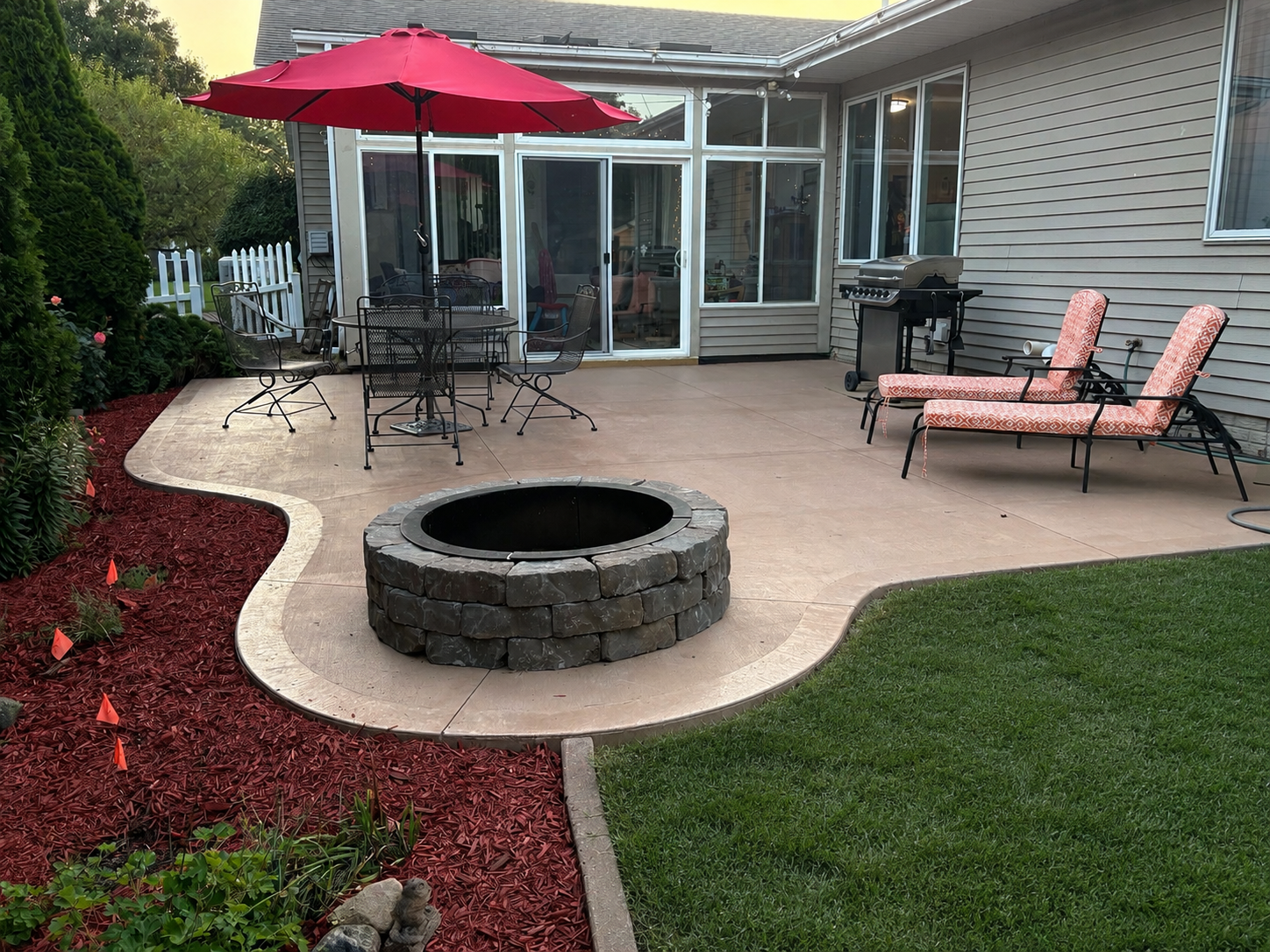 A backyard patio with a fire pit, patio furniture, a barbecue grill, and a screened-in porch in the background.