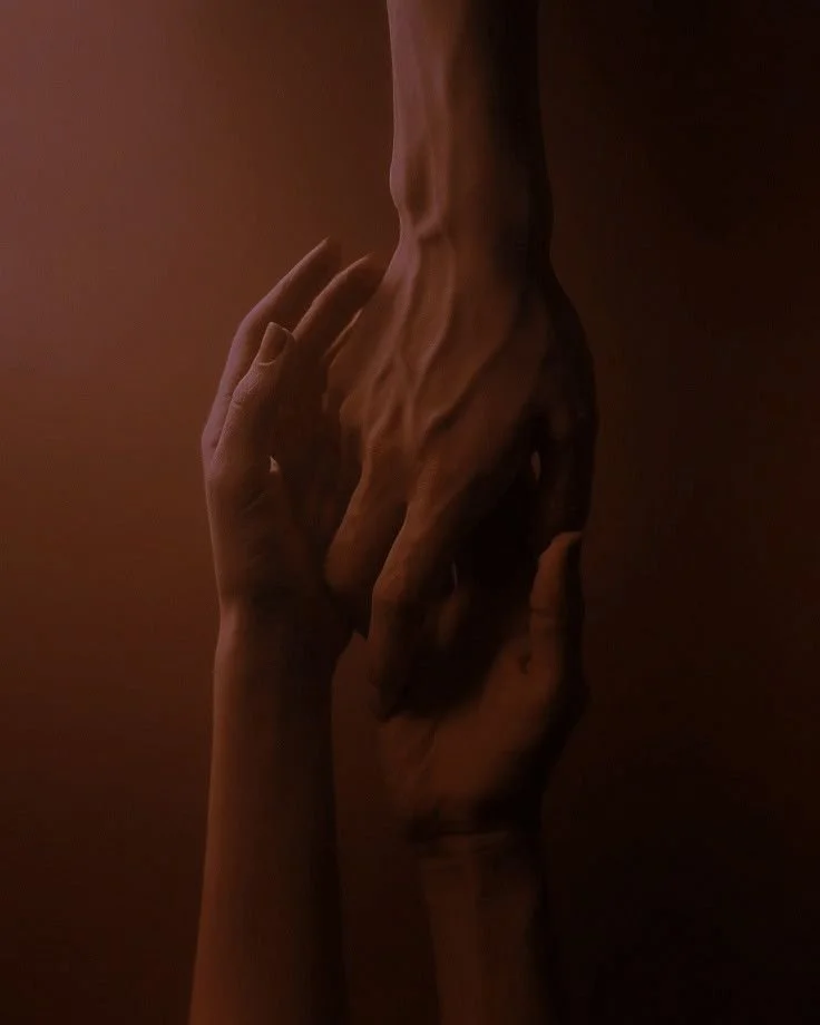 Two human hands, one darker and one lighter, gently touching and holding each other in a tender manner, set against a dark brown background.