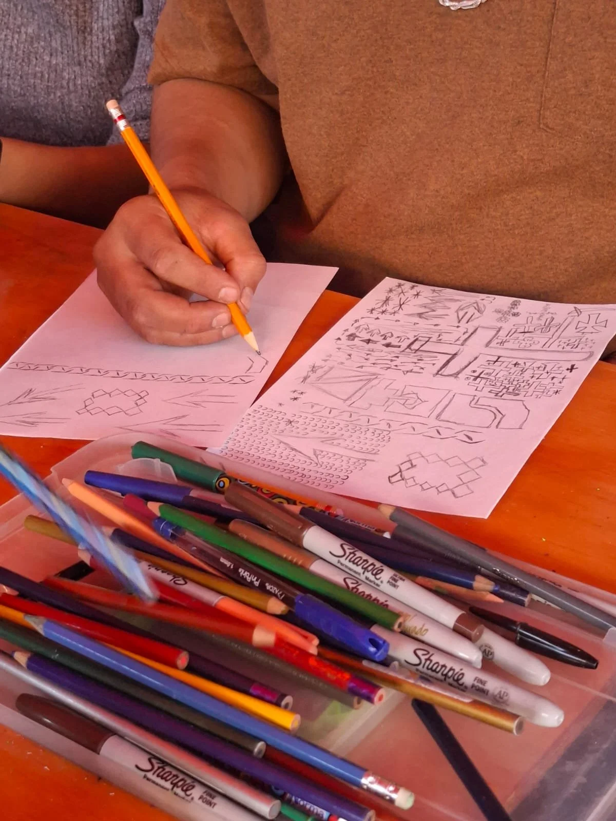Personas dibujando en papeles con lápices y bolígrafos de colores en una mesa de madera