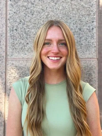 Blonde-haired woman who is smiling against a granite stone background.