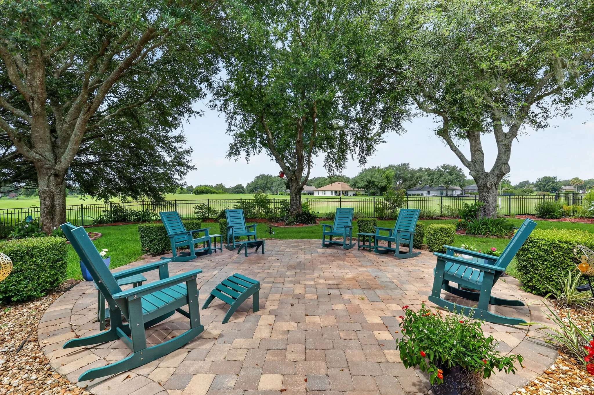 Backyard patio with blue chairs arranged around it, green trees, and a view of houses in the distance under a blue sky.
