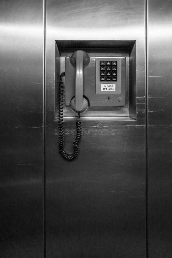 A wall-mounted telephone with a keypad and a small display, set in a metallic wall.