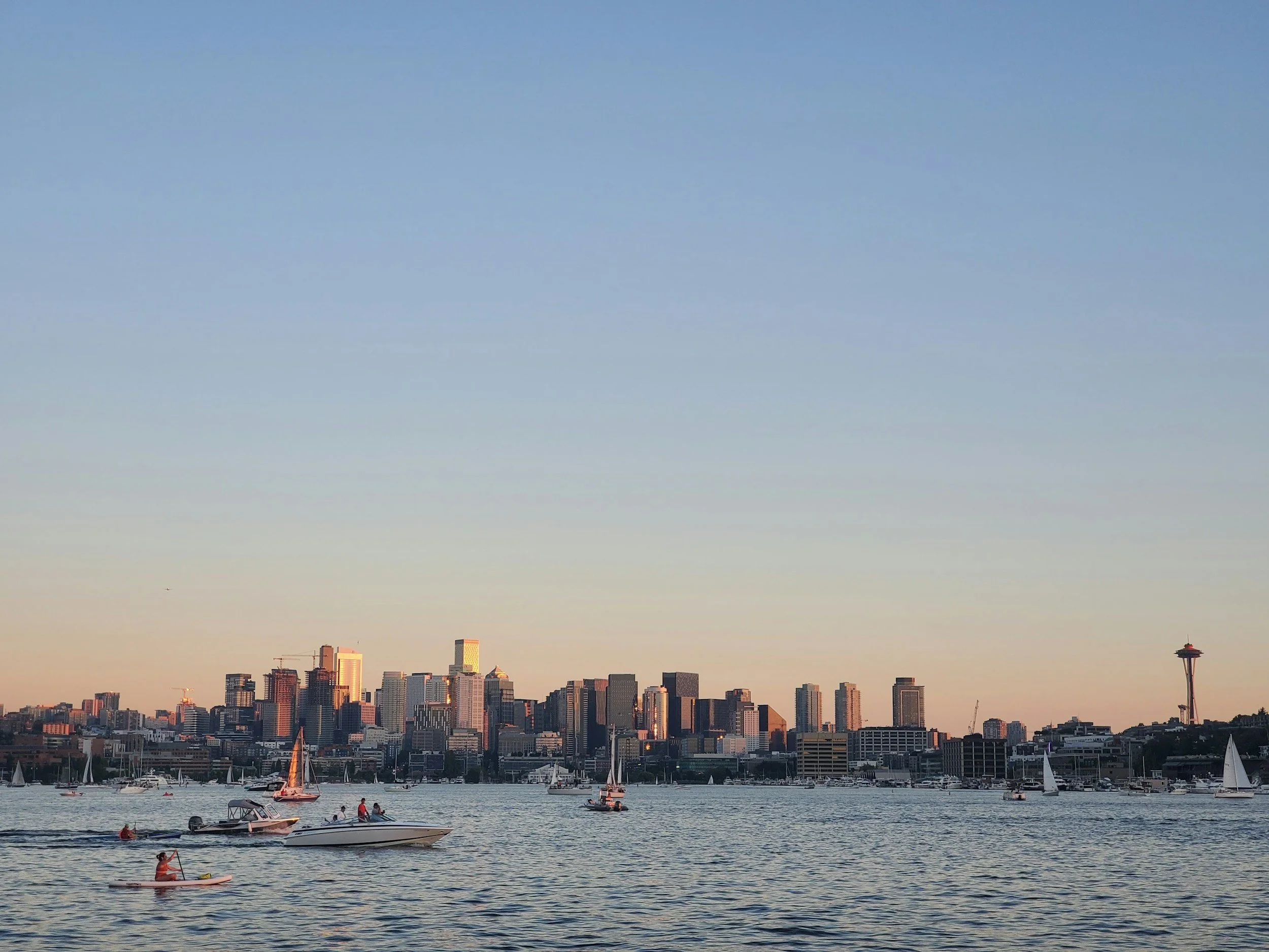 View of Seattle skyline during sunset with boats and kayaks on the water in the foreground.