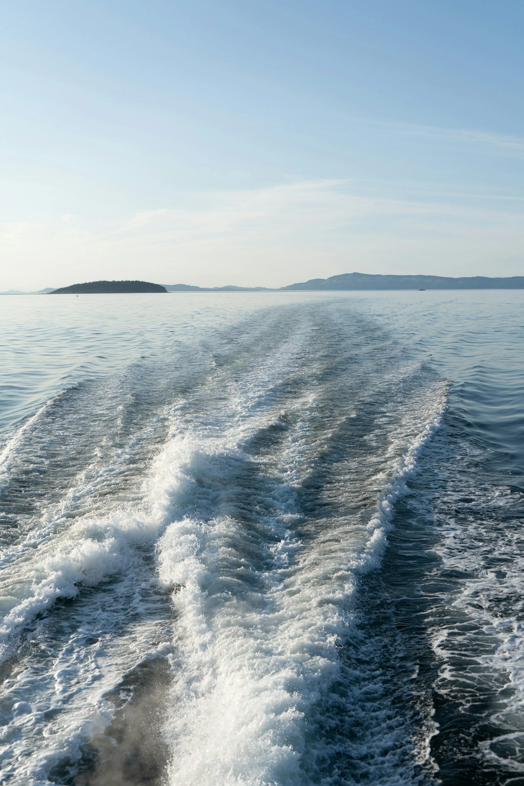 A view of a boat moving through the water, creating a wake behind it, with distant islands and a clear sky in the background.