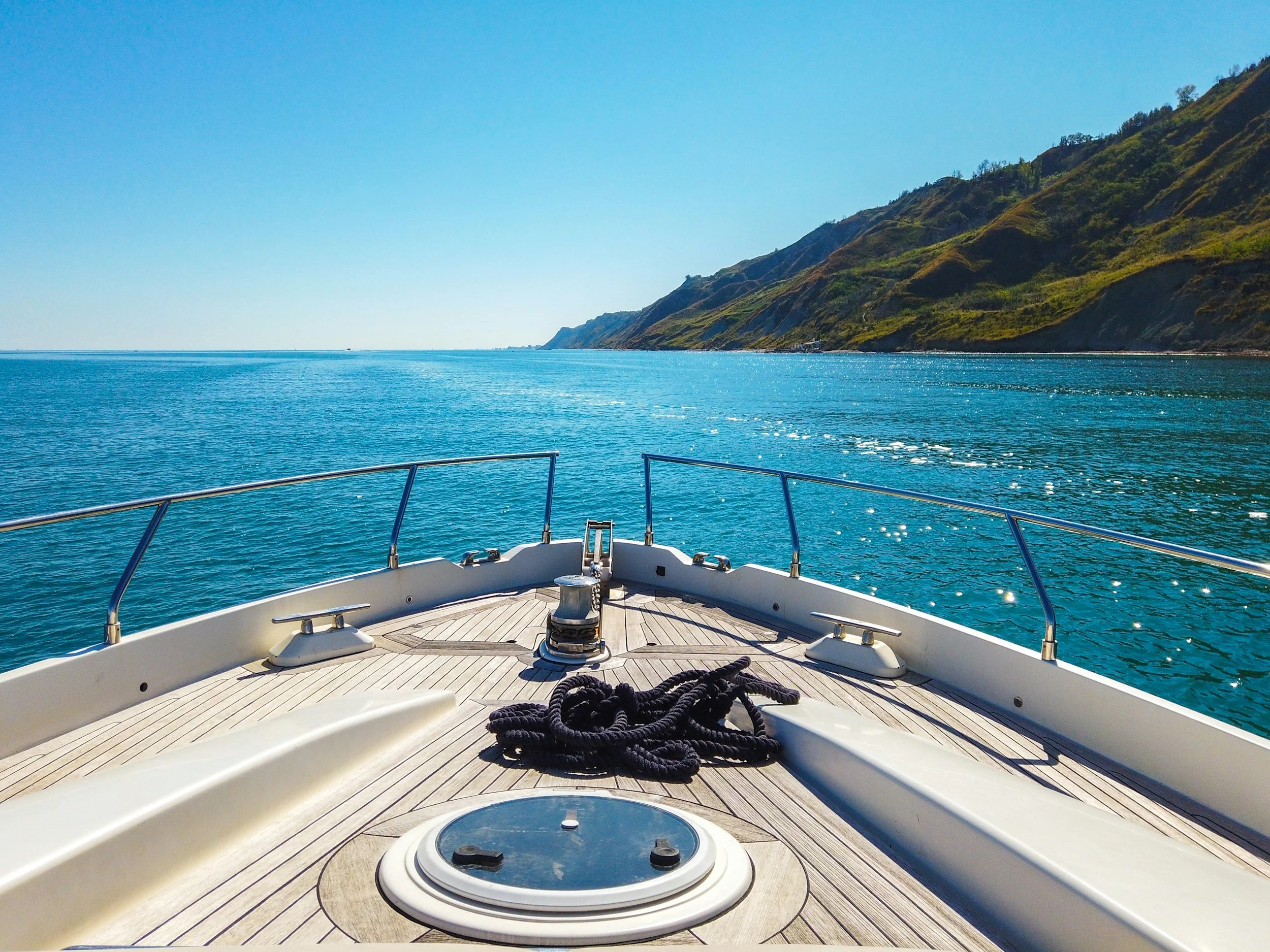 View from the deck of a boat showing blue water and distant green hills with clear sky.