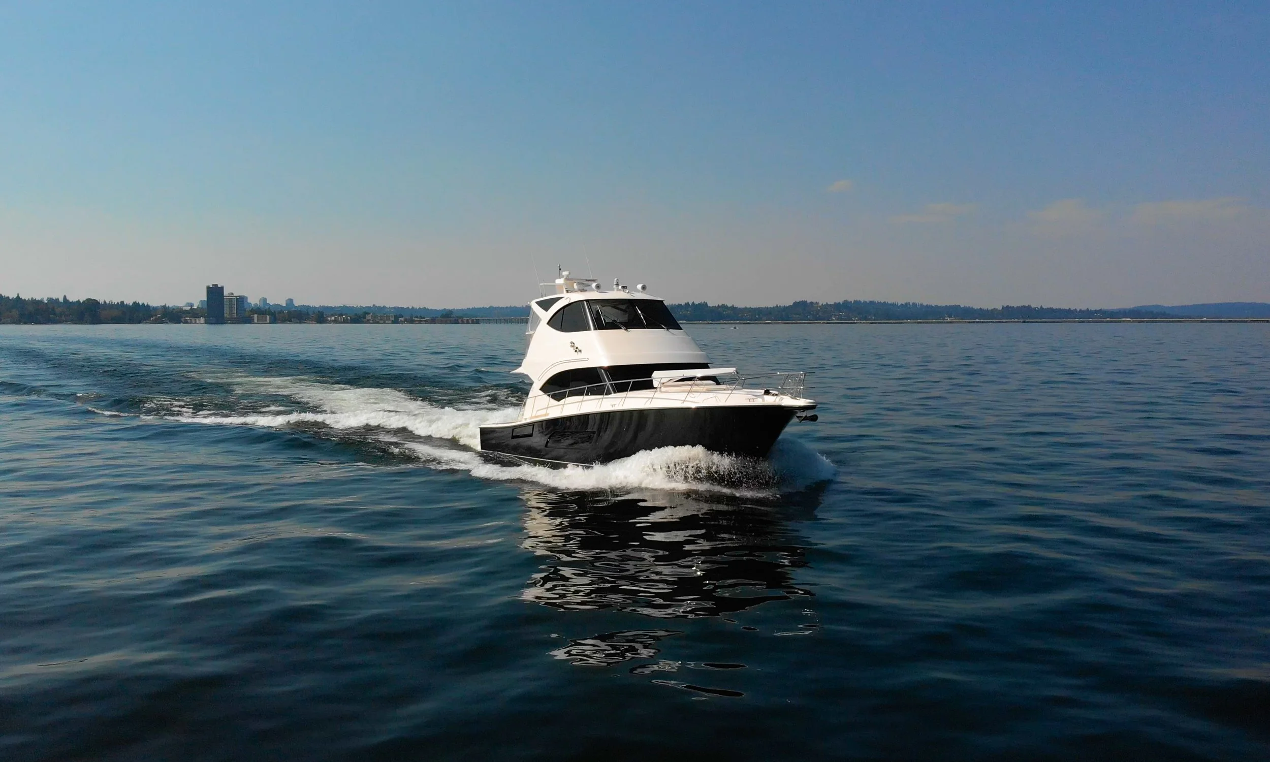 Aerial view of a white motor yacht cruising on the open ocean with a wake behind it, under clear blue waters.