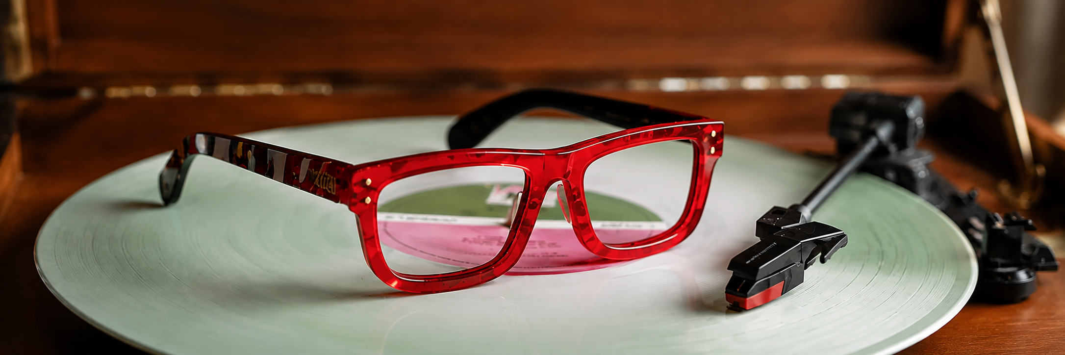 Red tortoiseshell glasses on a green vinyl record with a turntable in the background.